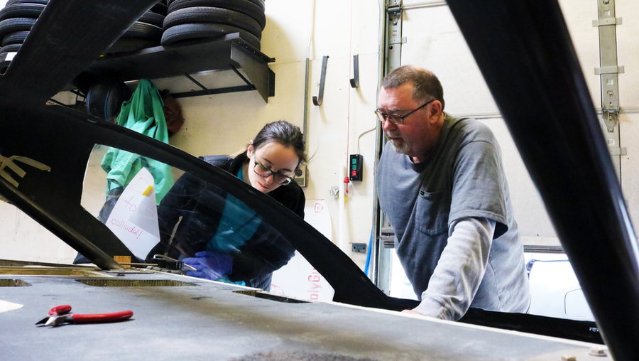 Pat McAtamney leans on car while a student inspects the front suspension.