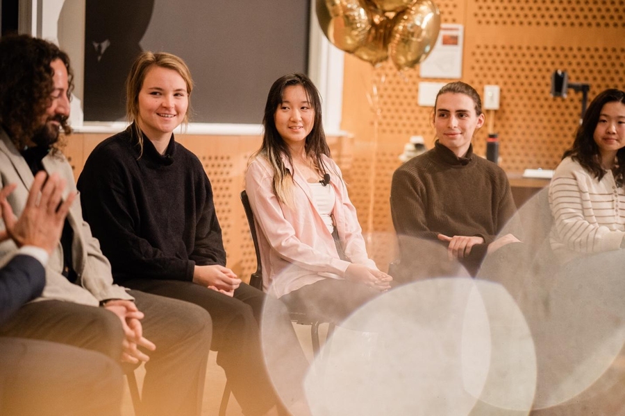 Joe Diaz, Rachael Harkavy, Joyce Yuan, Lancelot Blanchard, and Grace Song are all seated in a row in front of an audience, smiling and listening intently to someone out of the frame.