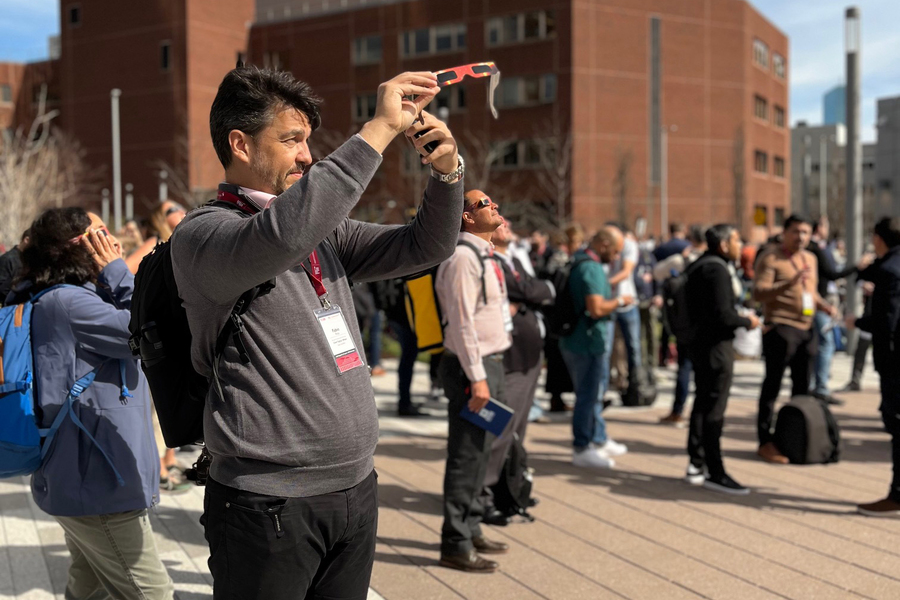 A man looks at the eclipse through his phone’s screen, with many eclipse watchers in background.