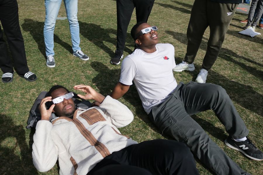 2 people lie on the grass while wearing eclipse glasses
