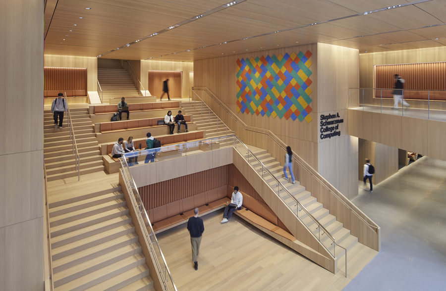 People sitting on benches in the center of a lobby that is framed by stairs to the left and right.