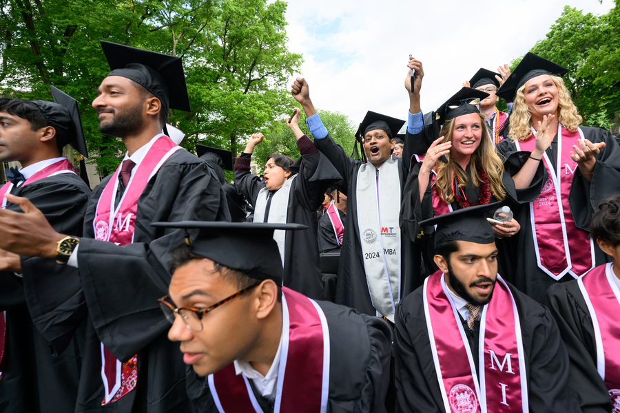 A group of graduates wearing caps and gowns cheer on Killian Court.