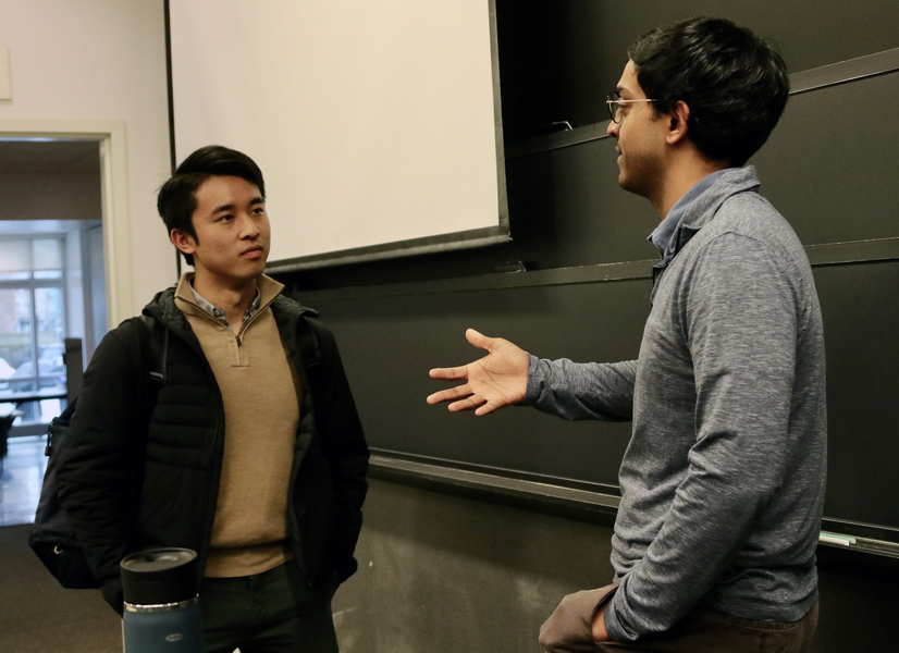Ashesh Rambachan converses with Jimmy Lin in the front of a classroom.