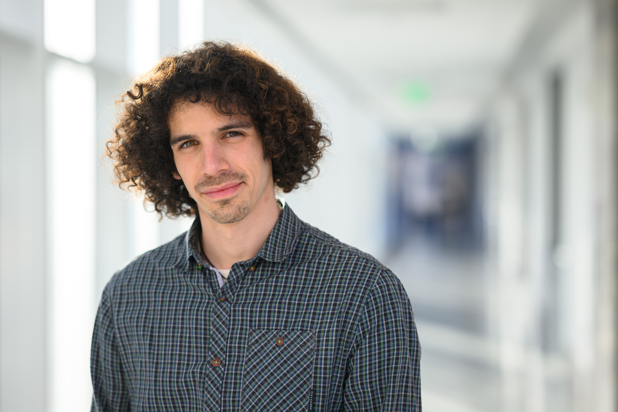 Eli Sanchez stands in a naturally lit, out-of-focus hallway