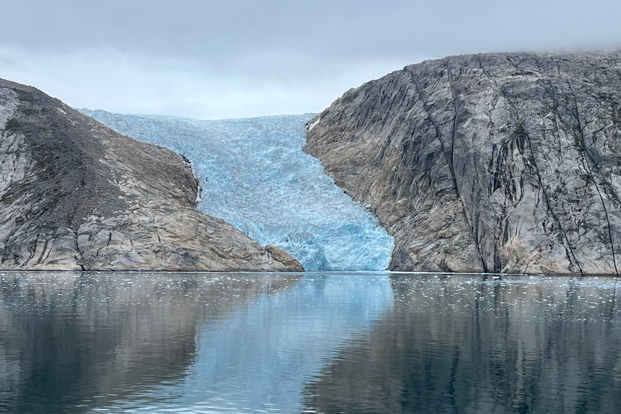 In between two rocky hills, an icy blue glacier flows down and meets the water. 