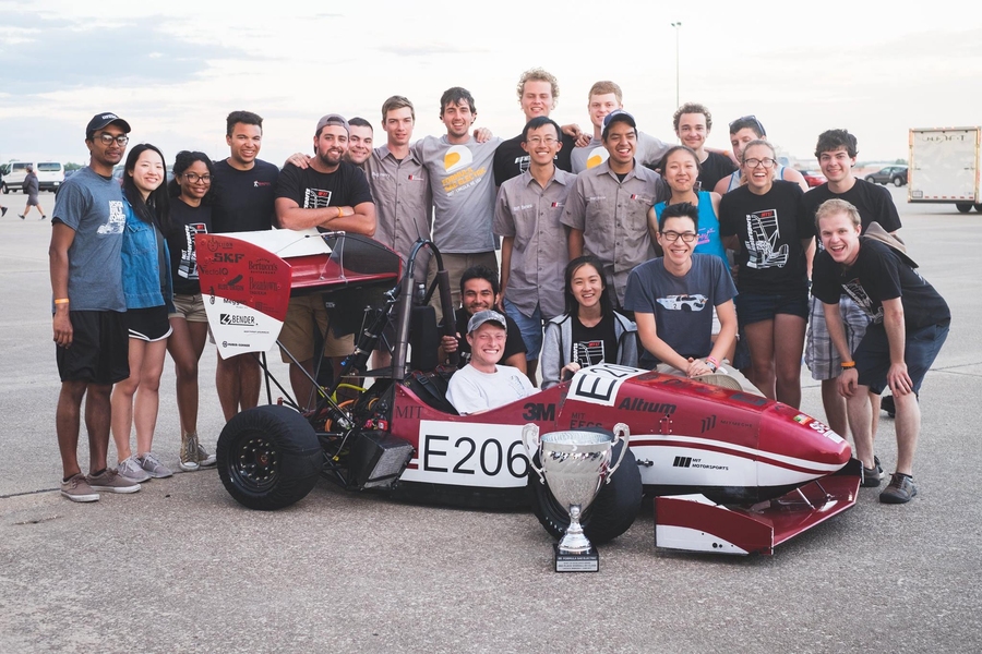 About 22 MIT Motorsports team members pose around their car and silver trophy