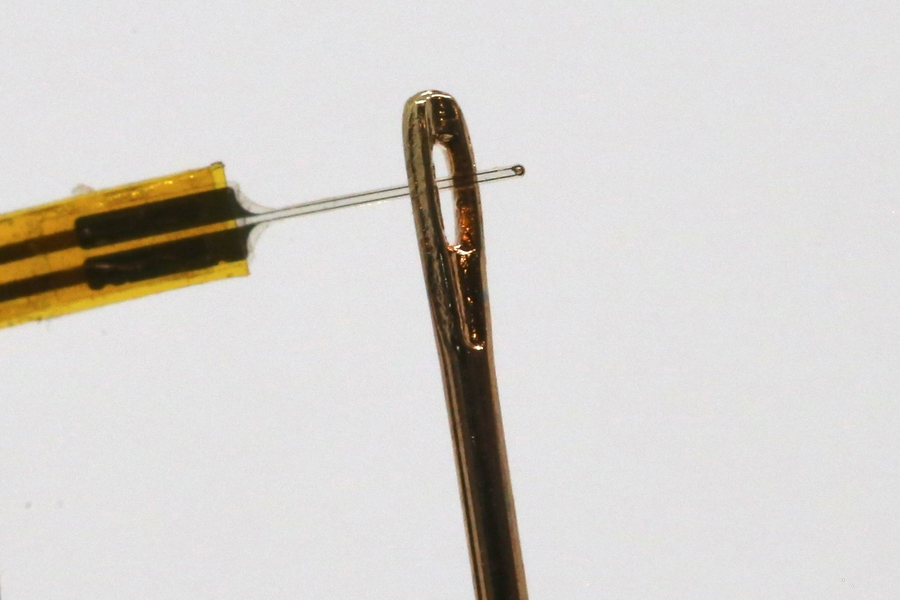 Close-up photo of a thin fiber being guided through the opening of a sewing needle.