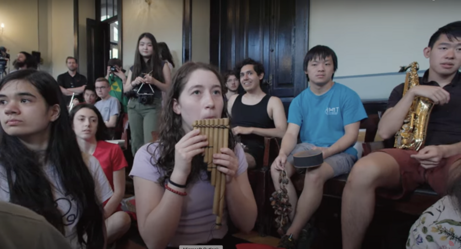 MIT students and others sit together, several holding or playing musical instruments.