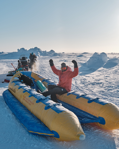 A person rides on an inflatable slide towed by a snowmobile. 