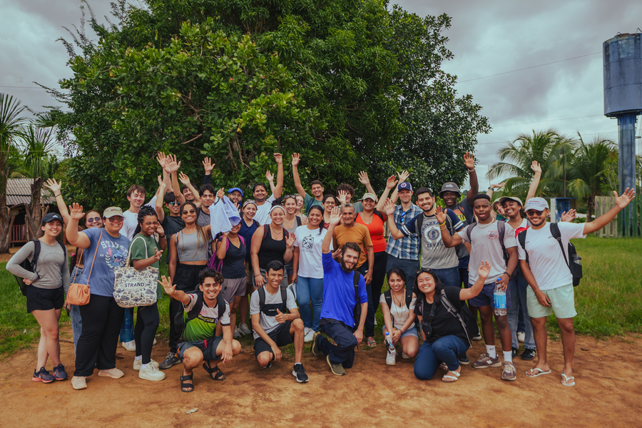 About 35 happy people pose for a photo with their hands raised.