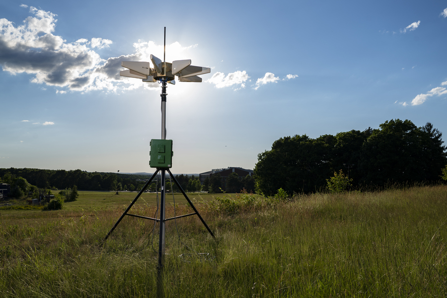 An antenna array atop a tripod is set up in a field. 