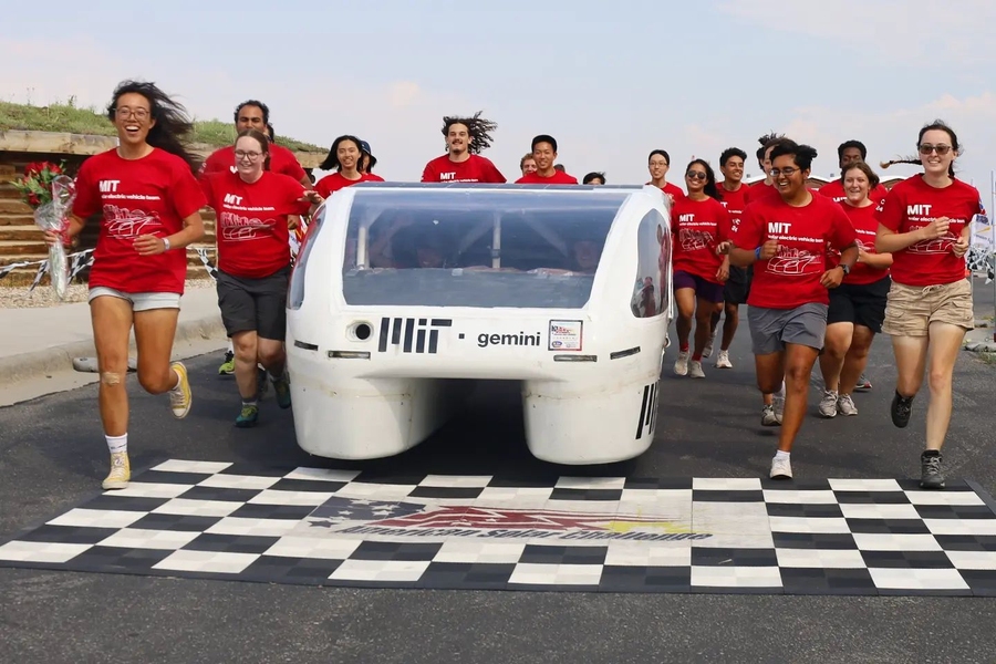 The Solar Electric Vehicle Team in red team shirts run across a checkerboarded finish line