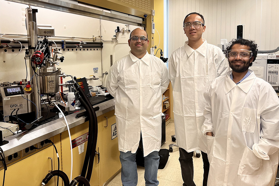 Ajinkya Pandit, Yi Wei, and Shashank Muddu pose in white lab coats and safety glasses next to a lab bench