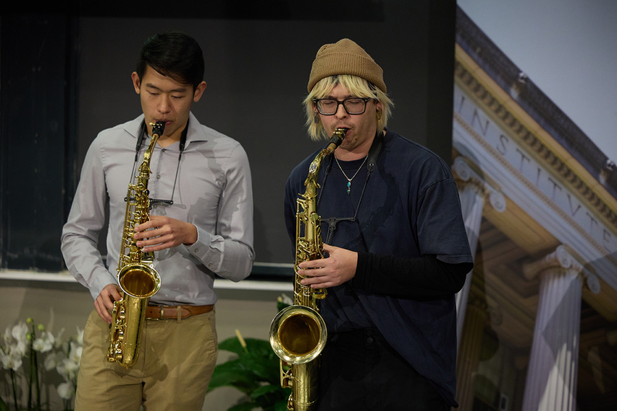 Two men play saxophone.