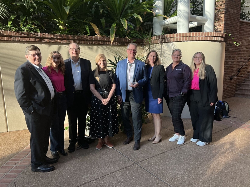 Eight people in casual business attire pose outdoors