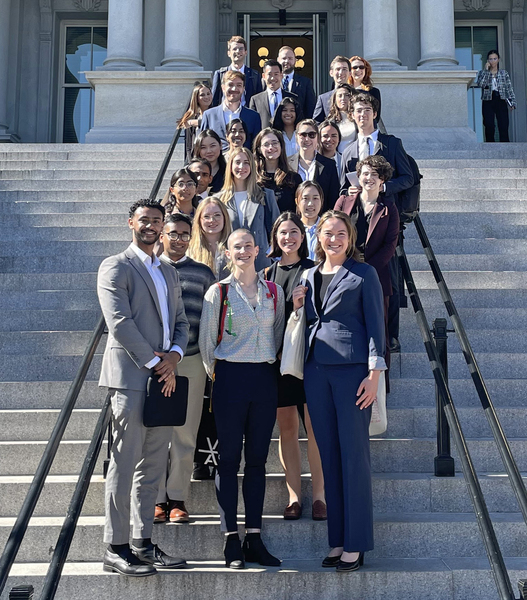 25 people pose on the stairs outside a colonaded portico