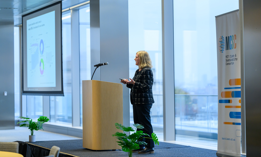 Caitlin Mueller speaks at a lectern in front of a wall of windows