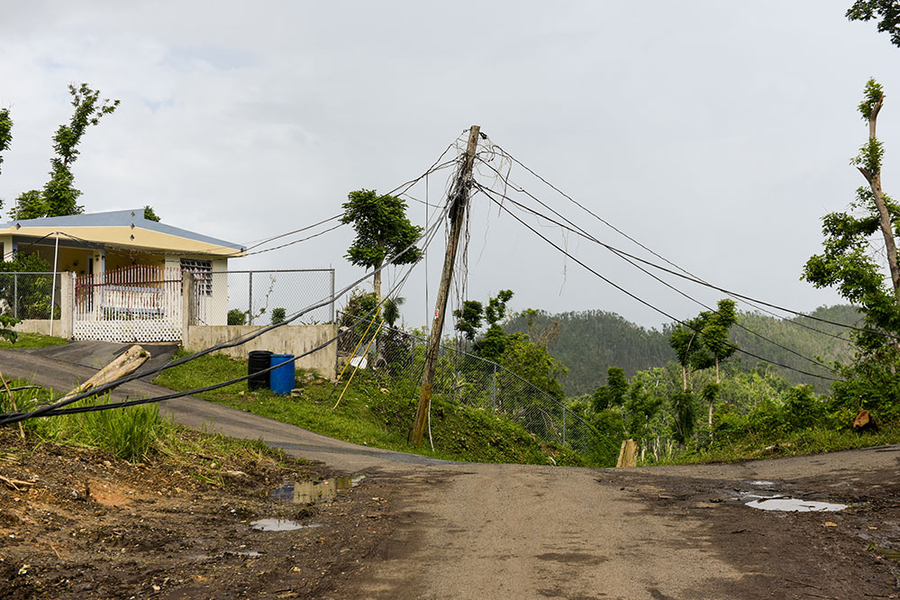 Down power lines at the center of a dirt road with partial view of a house in the upper left corner.