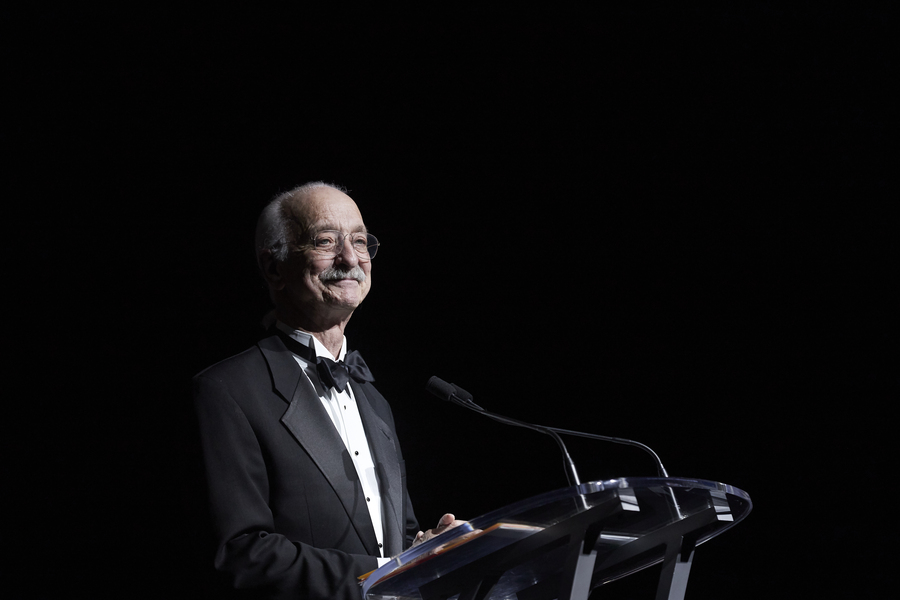 Woodie Flowers, dressed in a tuxedo, stands at a podium with a microphone