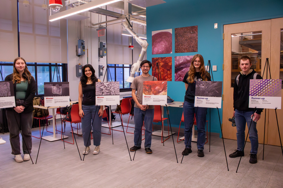 Five students who won an image competition stand next to easels holding their images.
