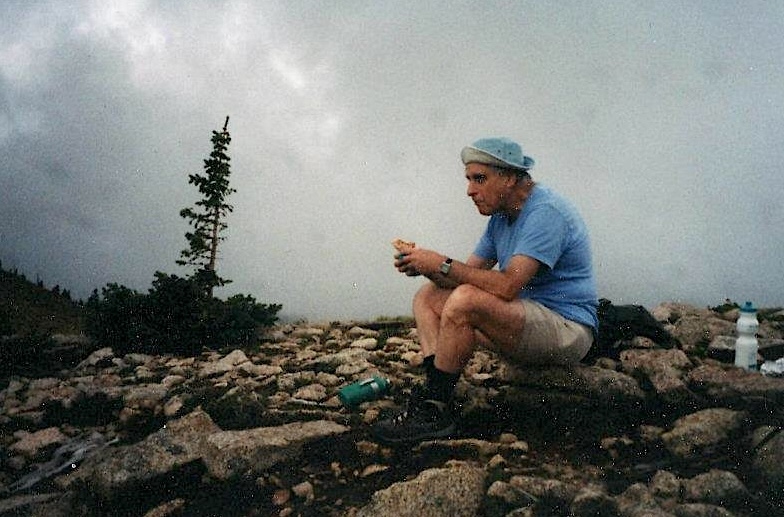 Lomon, in shorts and a T-shirt, enjoys a sandwich on a mountain top on a gray day