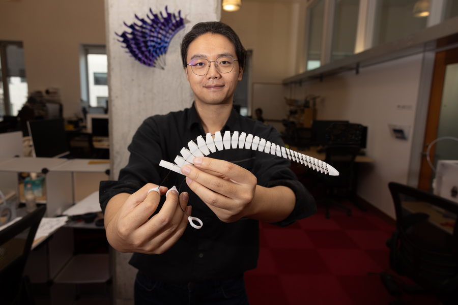 MIT researcher holds up a segmented white tentacle with a cable through its center.