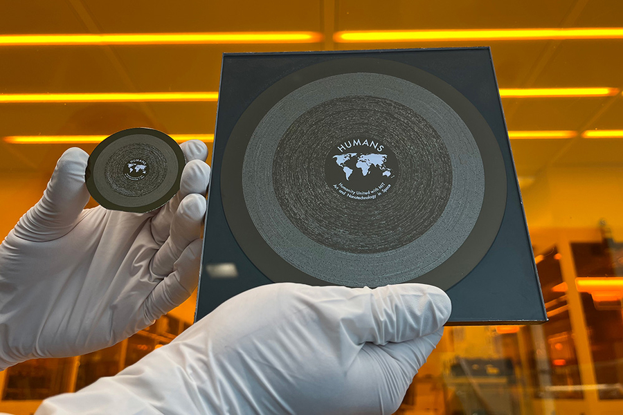 Two gloved hands, each holding a silicon wafer, one 6 inches wide, one 2 inches wide, in a lab