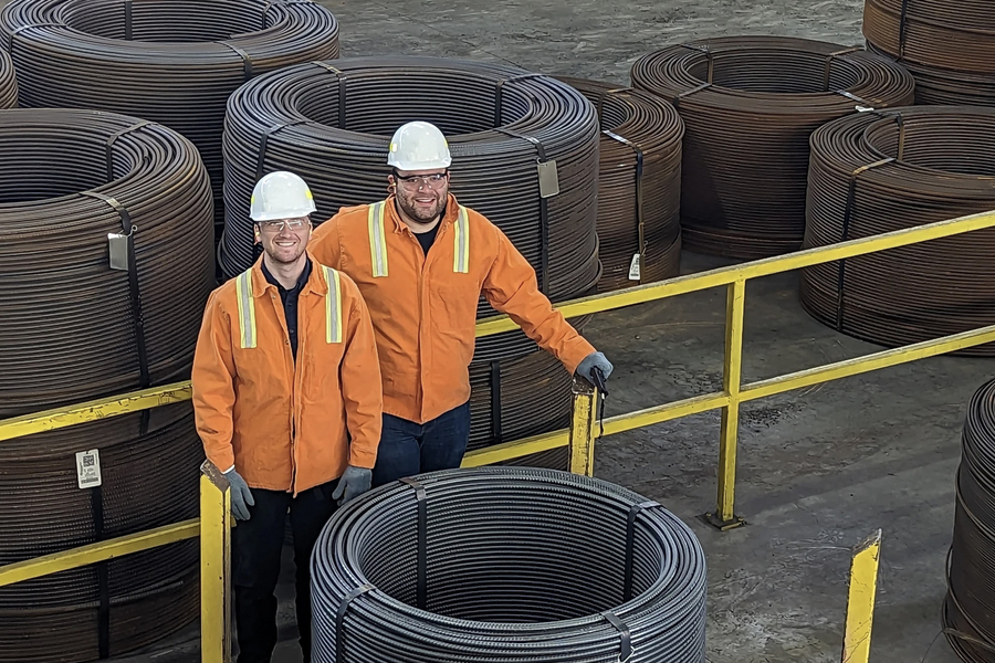 Sam McAlpine and Steven Jepeal in hard hats and orange safety jackets, next to large piles of coiled rebar