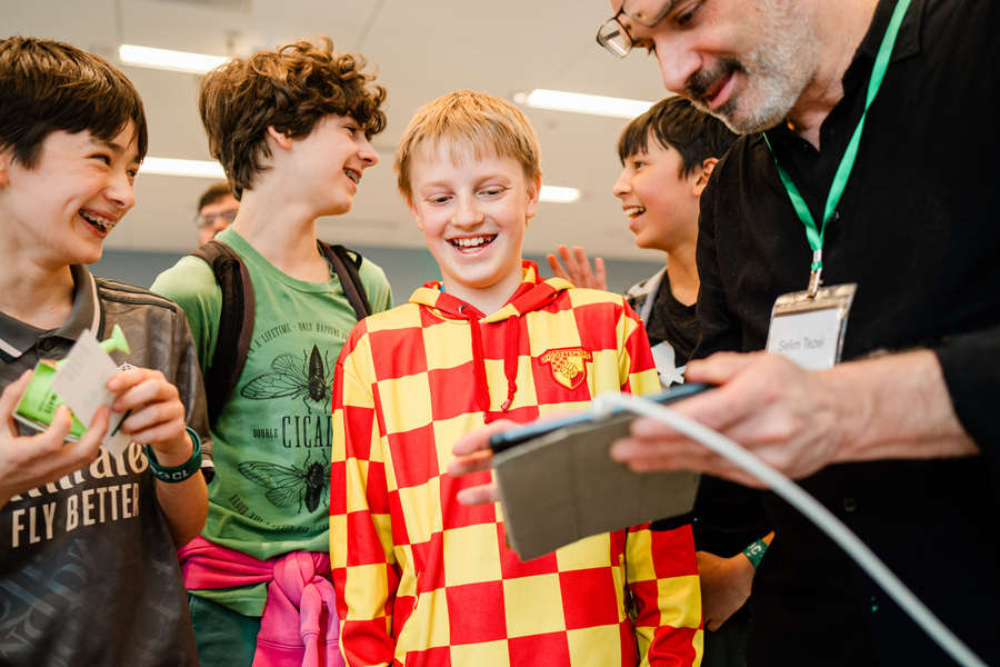 Four smiling students stand around a person holding a tablet computer