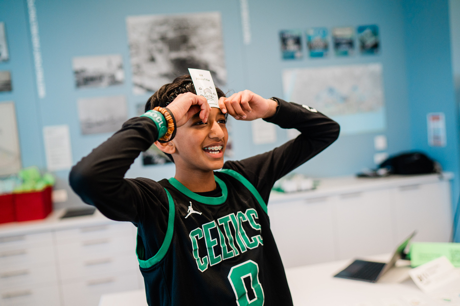 A boy wearing a Celtics jersey holds a card to his forehead 