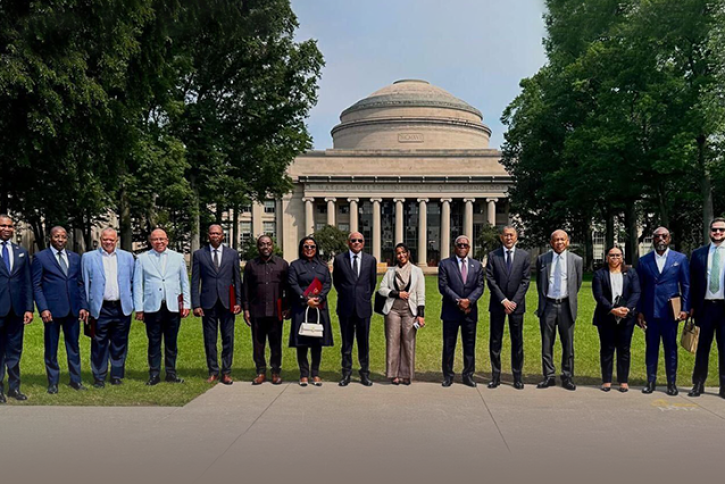 15 people in business clothing pose in a line in front of MIT’s Great Dome