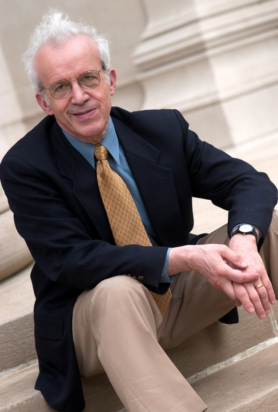 Daniel Kleppner poses, seated on stone steps with a stone column behind him