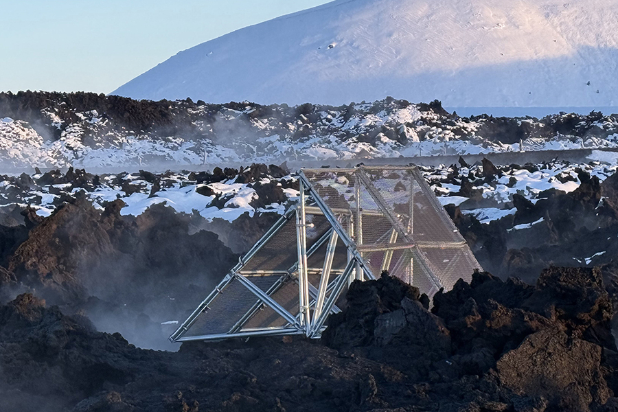Triangular metal framework object with two sides covered in mesh next to a steaming caldera
