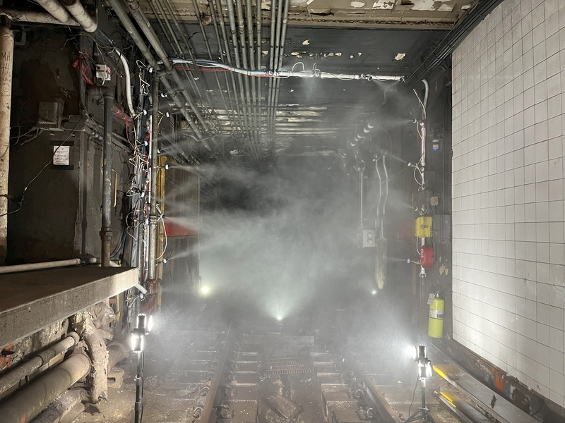 Image of spray nozzles protruding from both sides of a tunnel, spraying water in all directions across the opening.