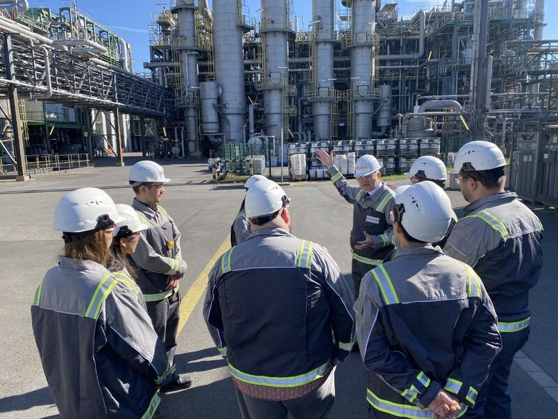 9 people in hard hats and safety gear stand outside a chemical plant