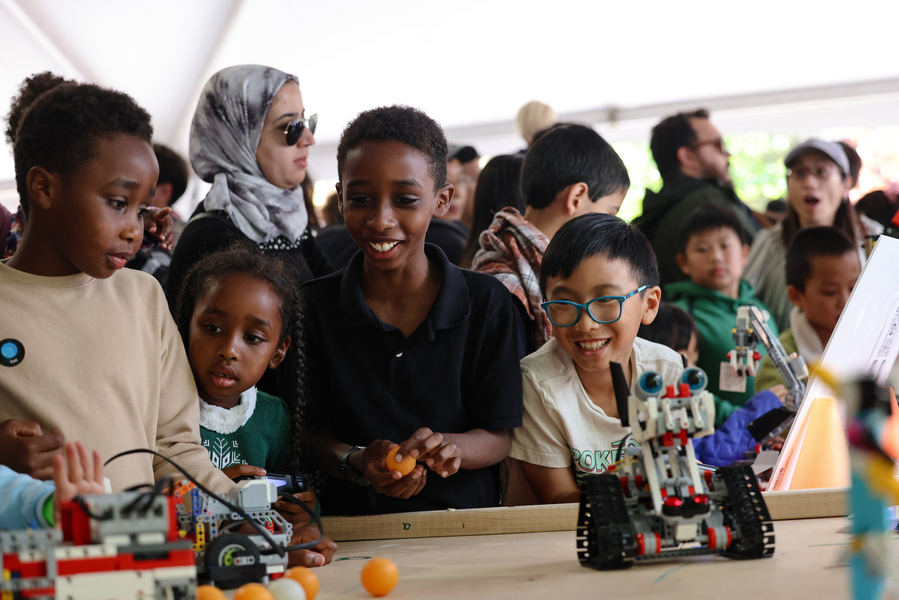Diverse group of 4 children watching tabletop robots in a crowded tent