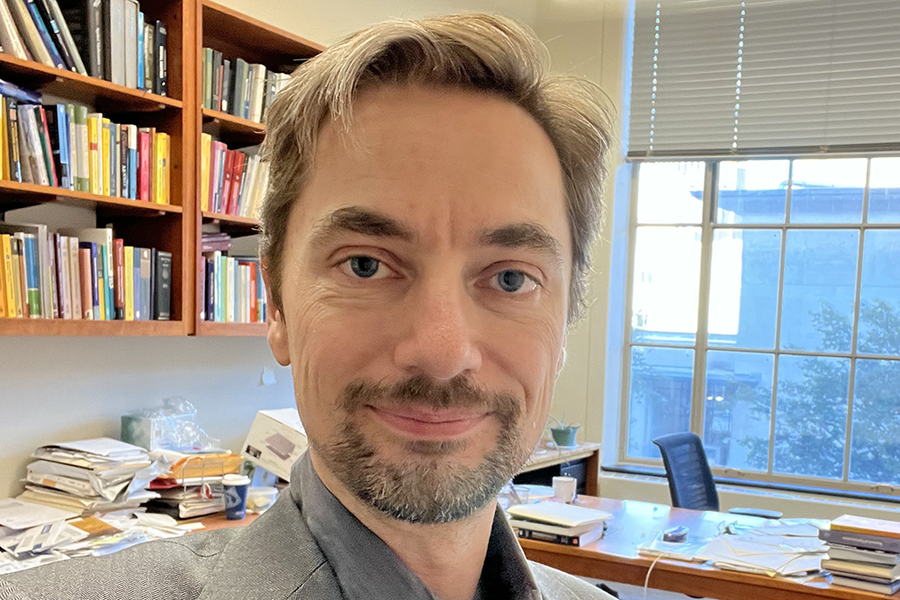Headshot of Laurent Demanet with bookshelf and window behind him