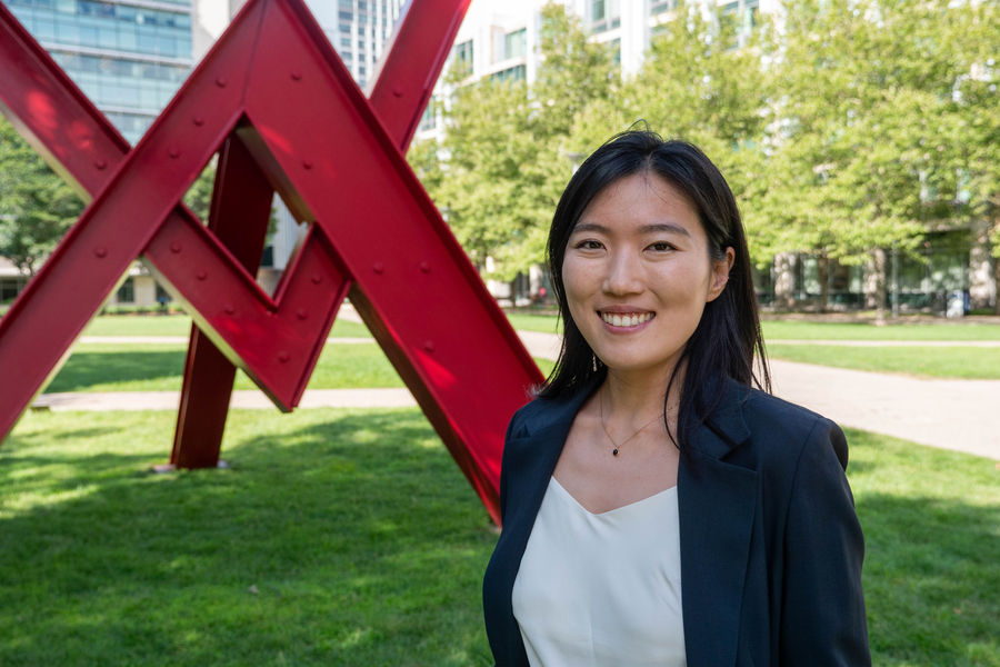 Yunha Hwang stands on Hockfield Court at MIT in front of a large, red sculpture fashioned from I-beams