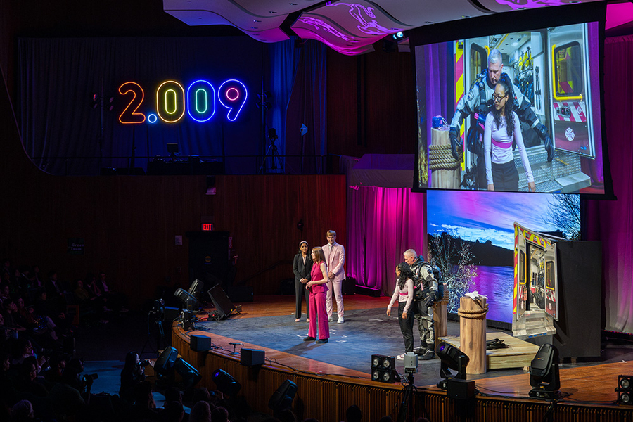 Wide shot of a stage. Two presenters demonstrate a device designed for rescue divers while three others look on.