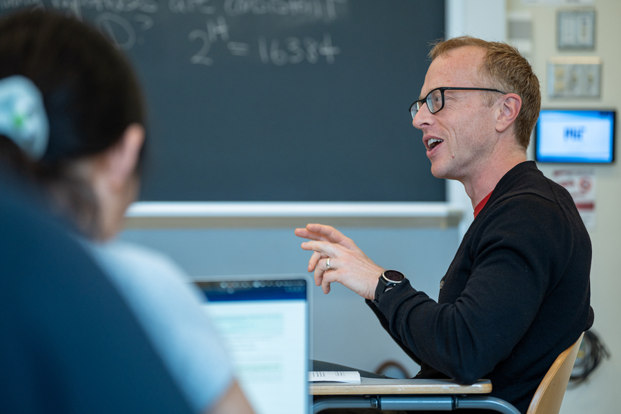 Profile view of Brian Hedden sitting with students, speaking to them.