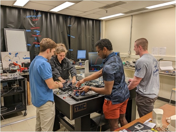 Four students stand around a table strewn with hardware.
