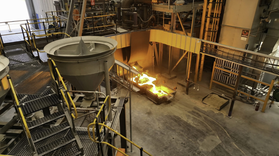 A wide photo of the plant shows large machinery on the second floor and molten steel flowing on the first.