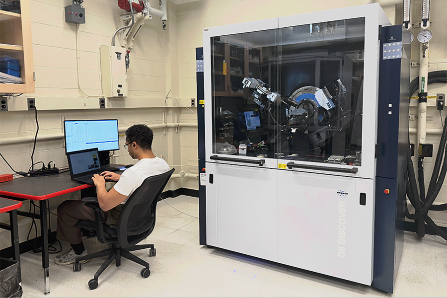 A person sits at a computer with a large x-ray diffractometer next to them.