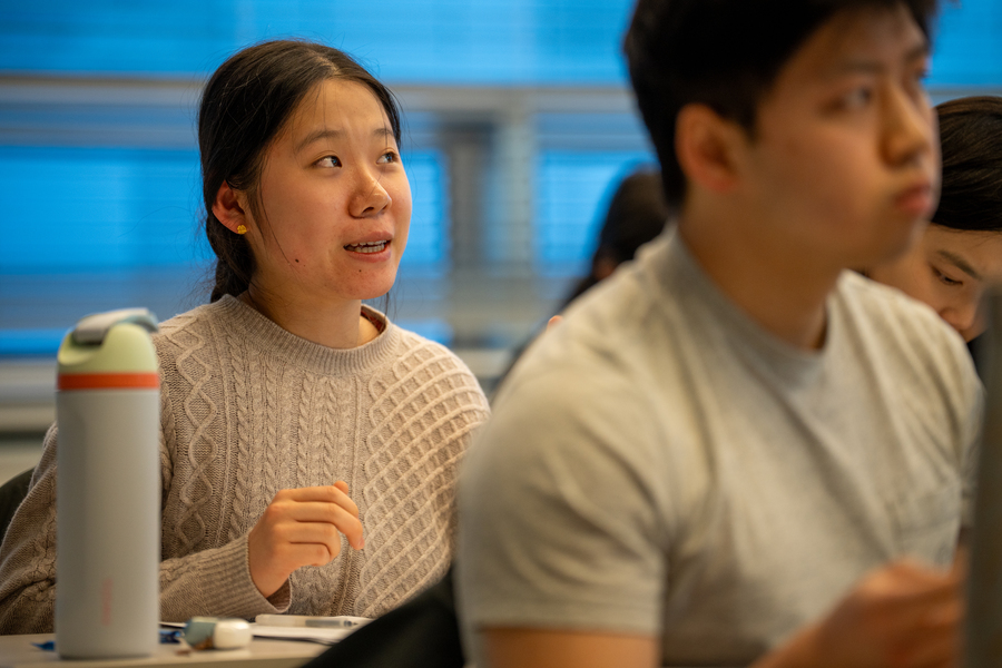 Close-up of four students seated at desks in a class, only one of whom is in focus