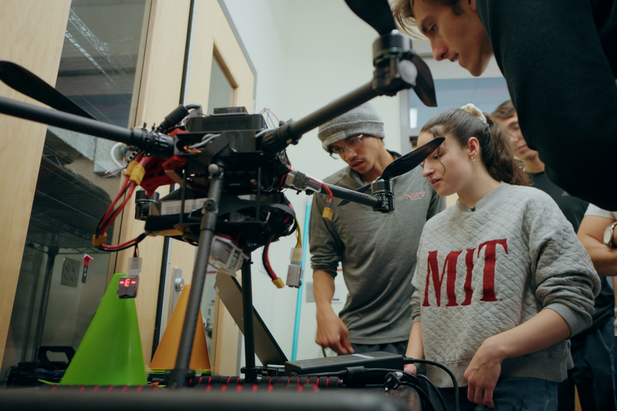 Three students examine a quadrotor drone in a workshop