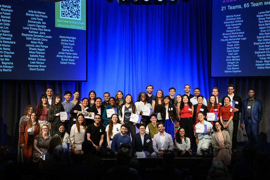 About 50 students pose for a group photo on an indoor stage. Many hold certificates.
