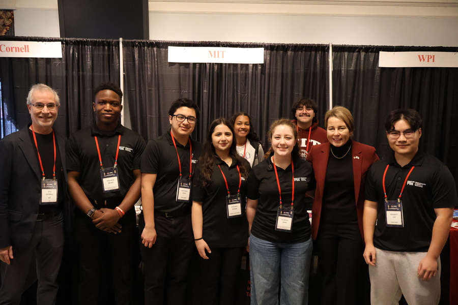 7 MIT students, all wearing lanyards, pose with Governor Maura Healey and MIT’s dean of admissions