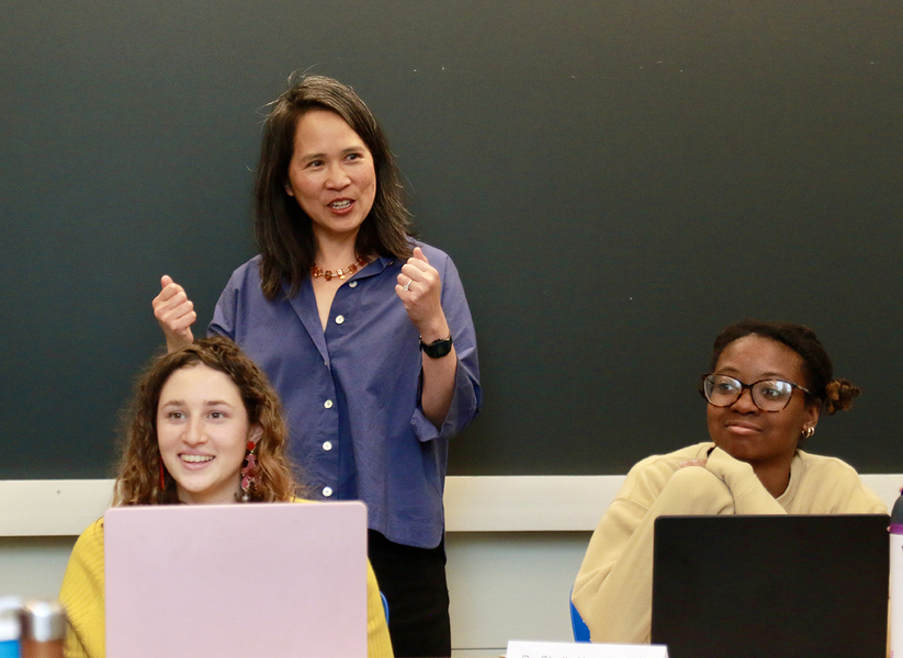 Professor Lily Tsai speaks behind two seated students with their laptops open