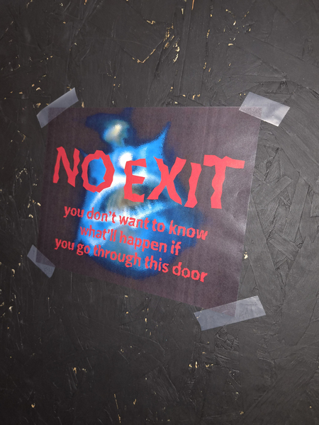 A sign with spooky font that reads: "No Exit - You don't want to know what'll happen if you go through this door" is taped to a black door