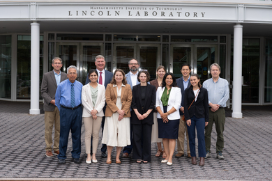12 individuals pose for a group photo outside of Lincoln Laboratory